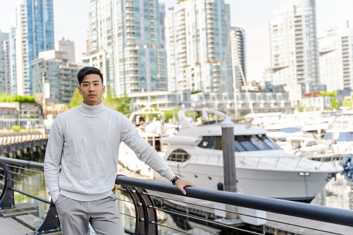 Attractive, handsome asian businessman standing near yacht in port, looking at camera. Serious chinese man posing for picture. Business concept