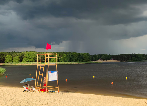 Cedzyna, Poland, 06/18/2023: Water lifeguards at a guarded swimming area with a red flag and a lifeguard tower during a storm