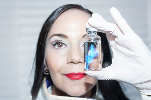 Doctor of biomolecular medicine scientist holds between her fingers a vial containing the double helix DNA elicitor with RNA copy human genetic copy vaccine
