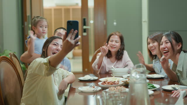 Asian multi-generation family reunion taking selfies photo while having a conversation and sharing stories at the dinner table in the front yard.