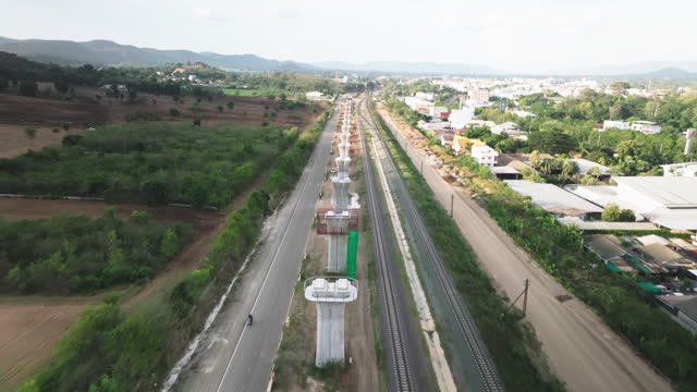 Aerial view of construction in progress of a mass rapid transit line, with a bridge girder erection machine working alongside a crane on the new highway or bridge under construction.