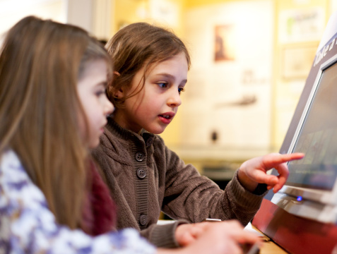 Two young girls are using a touch screen visual aid in a museum, Lyme Regis, Dorset, UK