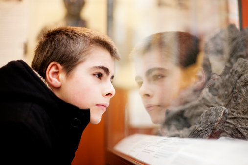 A young man looking at an exhibit in a glass display case in a museum, Lyme Regis, Dorset, UK