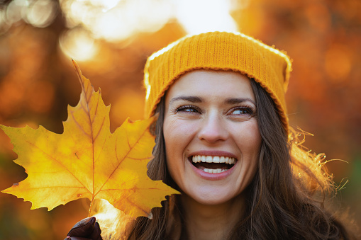 Hello september. smiling stylish female in brown coat and yellow hat with autumn yellow leaves outdoors in the city park in autumn.