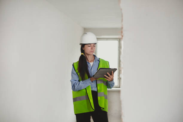 istock Female Industrial Engineer in White Hard Hat, High-Visibility Vest Working on Tablet Computer. Inspector or Safety Supervisor in construction site 1659760441