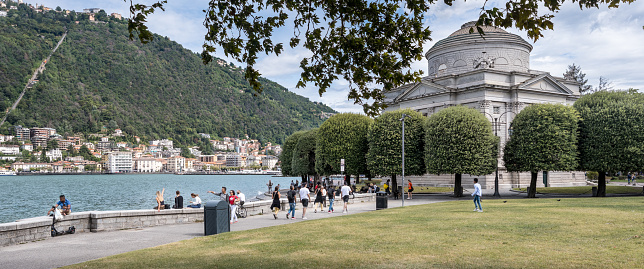 Como, Italy - 2023, August 29 : A lakeside public city park next to the Volta temple, a science museum dedicated to Alessandro Volta, and Brunate on the hill in the background
