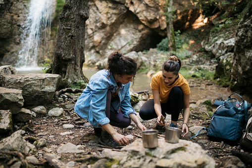 Two female hikers preparing campfire together for cooking on mountain trail. Two young women hikers preparing food on forest trail.