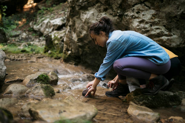 istock Woman hiker washing coffee cup in small mountains river while on forest hike 1659794181