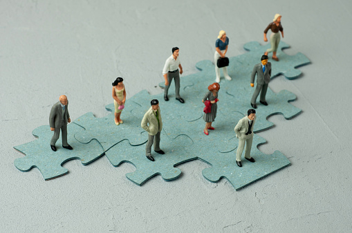 Business person figurines stand on a puzzle organization chart