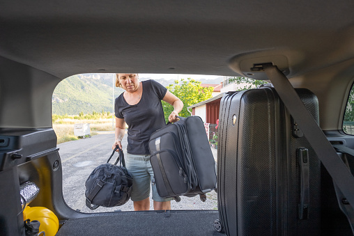 Mature woman loading her bags for the road trip in the trunk of the car.