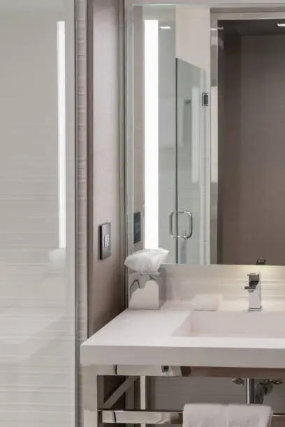 Interior of a modern hotel bathroom with a white sink, mirror, and glass shower