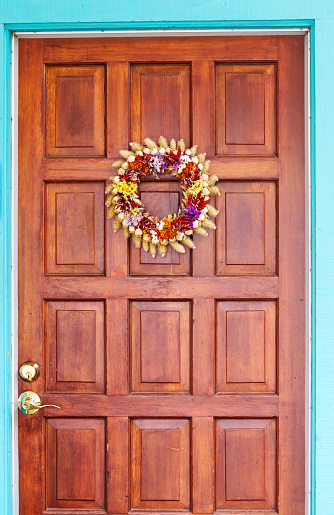 Wreath Of Dried Plants And Red Peppers Hanging On Wooden Door With Blue Frame