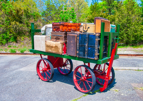 An antique railroad baggage cart loaded with vintage suitcases, trunks and valises at a Cape cod railroad station.