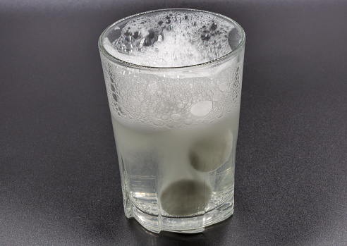 Dissolving instant effervescent tablets in a glass of water closeup on black