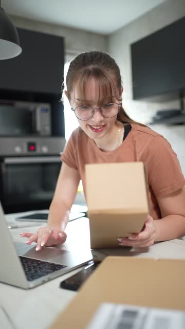 A young woman is checking a package at home that has just arrived for her, which she ordered online