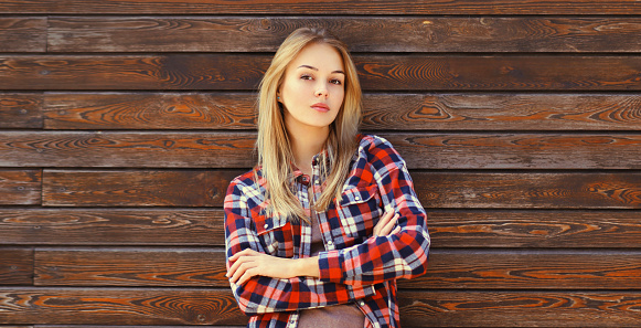 Portrait of beautiful confident caucasian blonde young woman with crossed arms in casual checkered shirt in the city