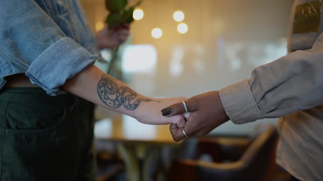 Close-up of lesbian couple holding hands and holding rose at coffee shop