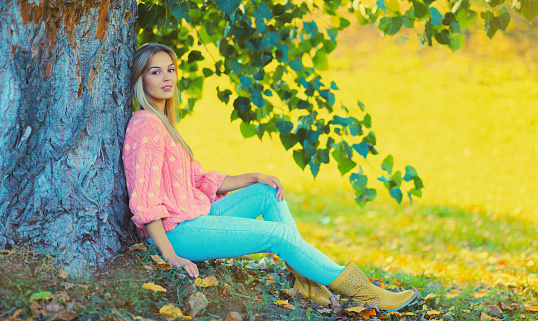 Beautiful young woman wearing pink sweater sitting in autumn park