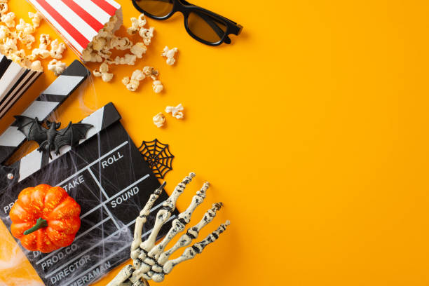 istock Embrace Halloween cinema vibe with thematic decor on orange backdrop. Top view spooky elements like skeletal hand, pumpkin, bat. 3D glasses, film clapper, popcorn boxes. Add text or ad in empty space 1659934341