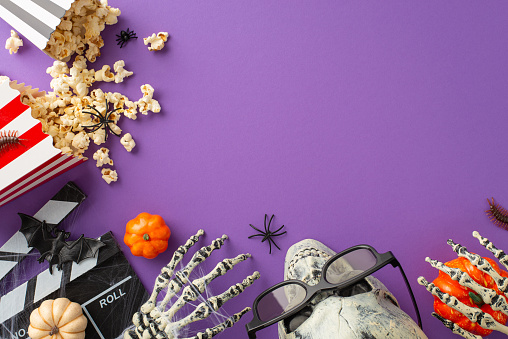 Indulge in spine-chilling Halloween thrills with a top-down snapshot of cinema popcorn and clapper surrounded by eerie decorations on a purple isolated backdrop, ready for your promotional messages