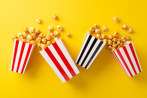 Film Entertainment Theme. Overhead shot of four striped boxes with tasty popcorn on a yellow backdrop, perfect for advertising or promotion