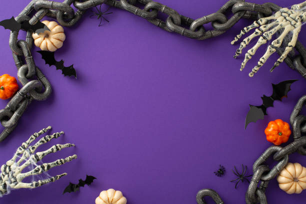 istock Enjoyable Halloween celebration concept. Top view photo featuring pumpkins, skeleton hands, chains and spooky decorations on a purple isolated backdrop. Ample copy-space for text or advertising 1659934892