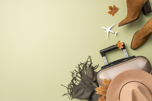 Fall vibes on plane adventure. Overhead shot of tiny aircraft, stylish elements including felt hat, scarf, western boots, gloves, suitcase, autumnal accents on soft green background with text space
