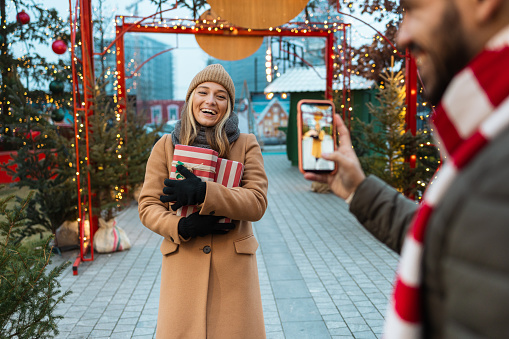 Young couple outdoors during Christmas. Young woman is posing with Christmas presents on a Christmas market.