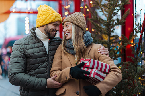 Young couple embracing on a Christmas market. They are looking at each other and smiling.