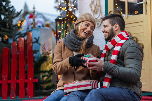 Young couple celebrating Christmas outdoors. They are exchanging presents