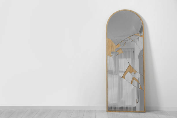 istock Broken mirror with many cracks near white wall indoors. Space for text 1659942814