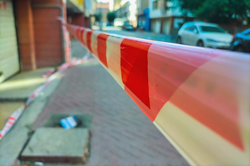 Red and white restrictive tape on the street, stretched to restrict access to this area of the street, yard. Element in criminal investigations, chronicle, news, construction work.