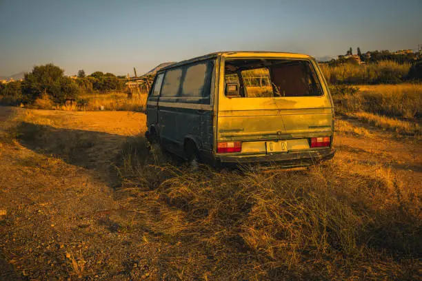Uncover the poignant tale of abandonment as the golden hour illuminates a forsaken green Volkswagen Transporter, nestled among the grasses on the roadside of Crete, a time-tinged memory frozen in time.