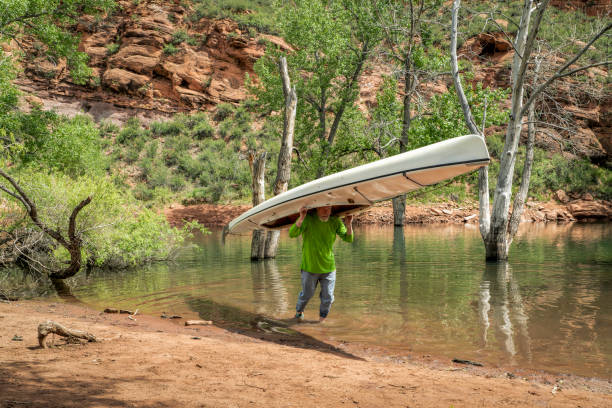 senior male is portaging a decked expedition canoe at foothills of northern Colorado in spring scenery
