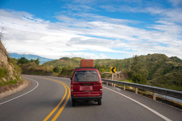Highway on mountain slope with a small red van with basket on the roof. Colombia