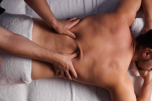 Handsome man having restorative back massage in spa salon, enjoying relaxing atmosphere, recharging after work. Masseuse gives therapeutic back massage to a visitor, the concept of healthy lifestyle.