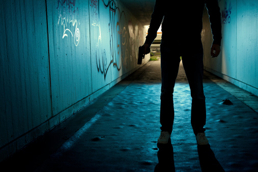 Man with revolver backlited in dark tunnel