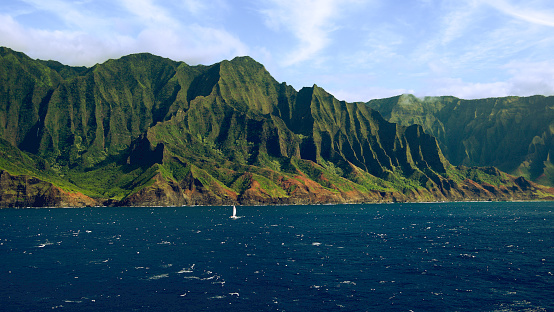 Ocean-level view of a sailboat sailing past the magnificent Napali Coast - Kauai, Hawaii
