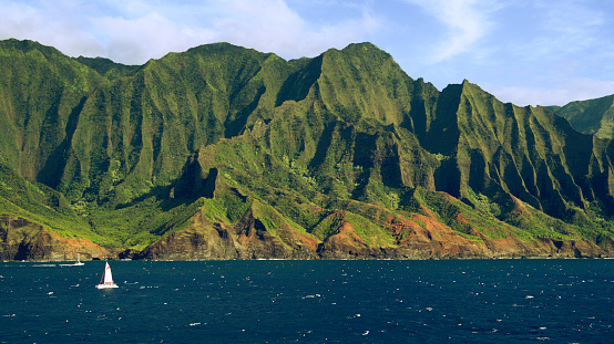 Ocean-level view of a sailboat sailing past the magnificent Napali Coast - Kauai, Hawaii