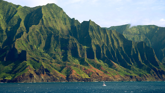 Ocean-level view of a sailboat sailing past the magnificent Napali Coast - Kauai, Hawaii