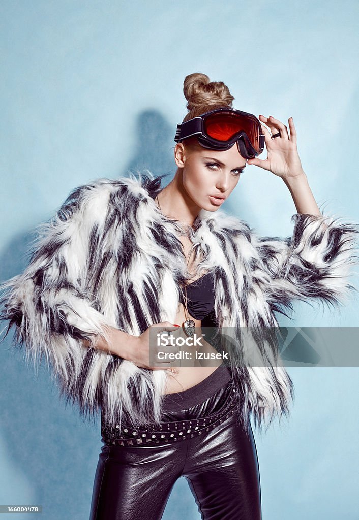 Fashion Woman, Winter Portrait Winter portrait of a stylish young woman wearing fur coat and goggles posing against blue background. Looking at camera. Studio shot. Bikini Stock Photo
