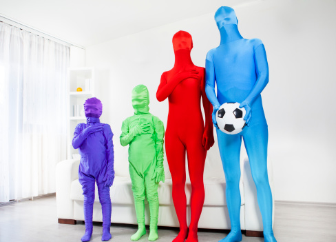 Family wearing color bodysuits and standing at home, listening the hymn. Unrecognizable people to show beauty of diversity and stop racism concept. Father holding ball.