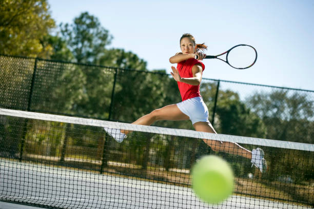 Tennis player hitting forehand winner low angle view of young woman hitting a big running forehand winner on hard court near the net. taking a shot sport stock pictures, royalty-free photos & images