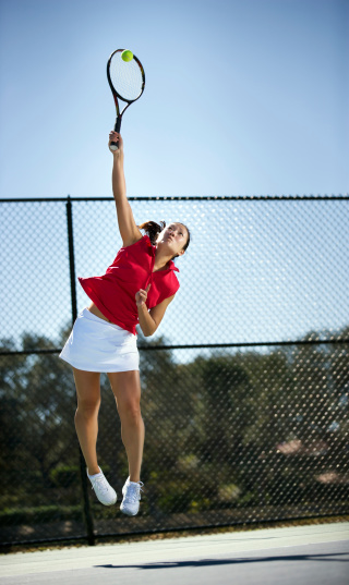 young Asian woman serving on hard court. High speed photography for stop action.