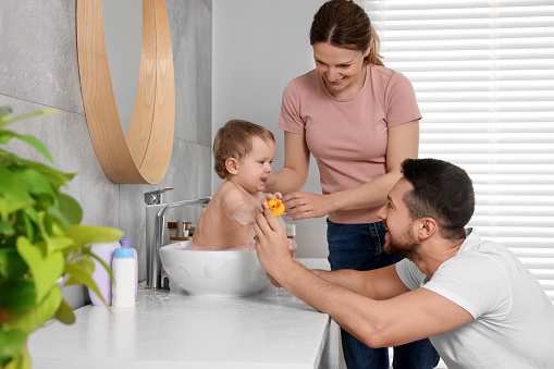 Father and mother washing their little baby in sink at home