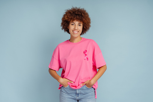 African American woman with pink ribbon isolated on blue background. Breast cancer awareness month