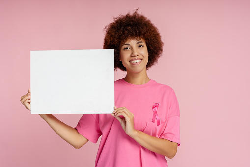 Smiling African American women with breast cancer pink ribbon holding empty banner isolated, mockup