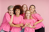 Smiling women wearing t shirts with pink ribbon isolated on pink background. Breast cancer