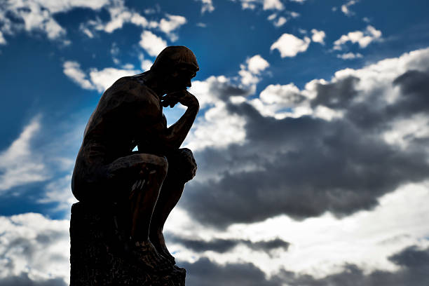 Replica of Rodin's The Thinker with sky background View of a small bronze replica of Rodin's The Thinker statue, with a dark, cloudy blue sky in the background.  The Thinker is often used to represent philiosphy. philosopher stock pictures, royalty-free photos & images