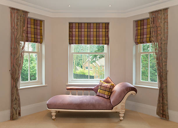 chaise longue in bay window a traditional pink chaise longue in the bay window of a girl's bedroom in a luxury new home. Matching silk cushions and blinds feature a pink and yellow pattern. The net drapes and wall covering also have hints of pink. chaise longue stock pictures, royalty-free photos & images